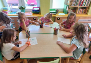 Dzieci siedzą przy stoliku i rysują obrazki.